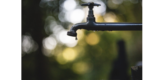Blurred background with water faucet in foreground dripping clean water