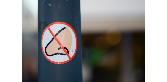 sticker with a nose covered by a red circle and diagonal line on a street post