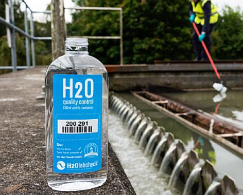 H2O Quality Control Bottle for wastewater assessment, wastewater treatment reservoir in the background