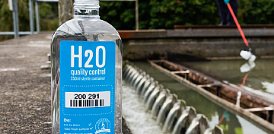H2O Quality Control Bottle for wastewater assessment, wastewater treatment reservoir in the background