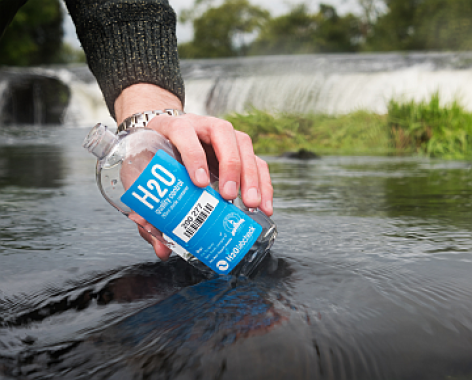 Hand pouring river water into sampling bottle